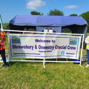 Two people standing either side of a large banner. The banner says 'Welcome to Shrewsbury and Oswestry Crucial Crew'