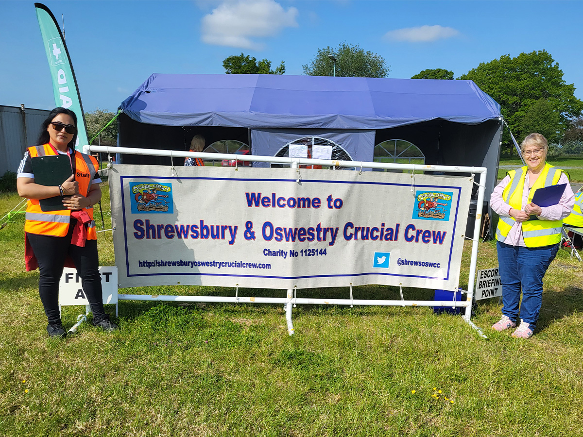 Two people standing either side of a large banner. The banner says 'Welcome to Shrewsbury and Oswestry Crucial Crew'
