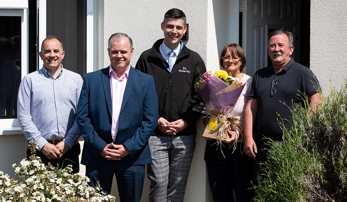 Five people are standing outside of a house, which has recently had maintenance work completed.